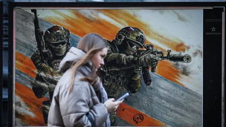 Alltag auch in Russland: Eine Frau geht an einem Plakat vorbei, das russische Soldaten in einer Ausstellung über den Ukrainekrieg zeigt.
