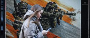 Alltag auch in Russland: Eine Frau geht an einem Plakat vorbei, das russische Soldaten in einer Ausstellung über den Ukrainekrieg zeigt.