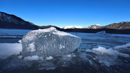 Ein Eisbrocken liegt auf dem mit einer Eisdecke überzogenen Eibsee unter strahlend blauem Himmel.