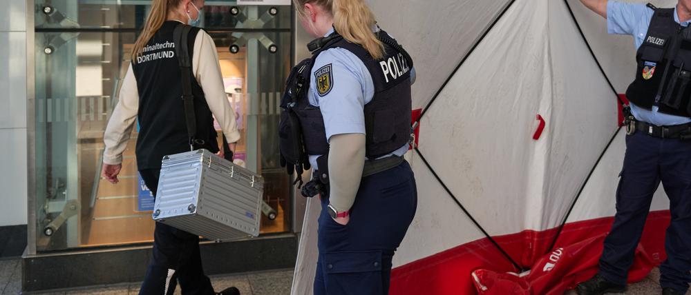 Polizisten öffnen den Sichtschutz vor einem Geschäft im Hauptbahnhof für eine Mitarbeiterin der Kriminaltechnik. Im Hauptbahnhof Dortmund ist am Mittag ein Mitarbeiter eines Fahrkartenschalters von einem Mann mit einem Messer angegriffen worden. 