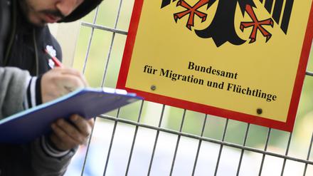 Ein Mann füllt ein Formular aus neben einem Schild vom Bundesamt für Migration und Flüchtlinge aus.