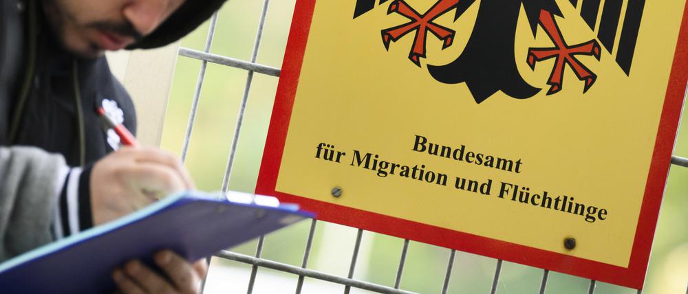 Ein Mann füllt ein Formular aus neben einem Schild vom Bundesamt für Migration und Flüchtlinge aus.