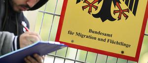 Ein Mann füllt ein Formular aus neben einem Schild vom Bundesamt für Migration und Flüchtlinge aus.