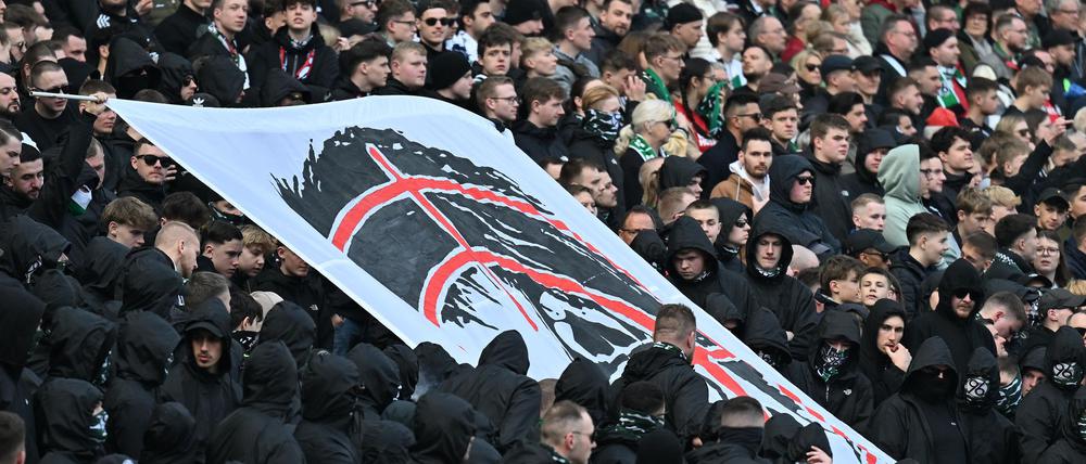 Hannover-Fans halten auf der Tribüne ein Plakat hoch, dass den Kopf von Niedersachsens Innenministerin Daniela Behrens in einem Fadenkreuz zeigt.