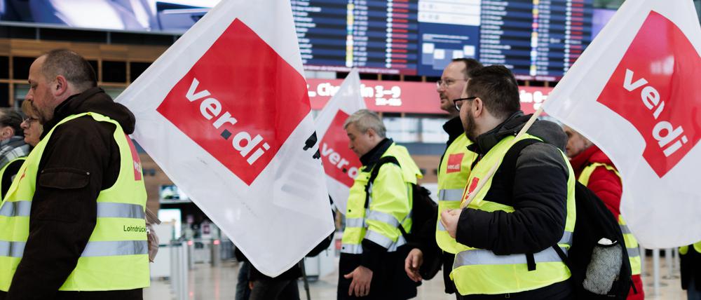 Mitarbeiter des Luftsicherheitspersonals demonstrieren mit Fahnen der Dienstleistungsgewerkschaft Verdi in der Abflughalle im Terminal 1 des Flughafens BER. 
