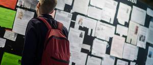Ein junger Mann mit Rucksack steht vor einer Wand mit Zetteln mit Zimmerangeboten.