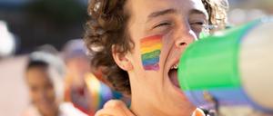 Junge Person mit Megaphon demonstriert für queere Rechte.