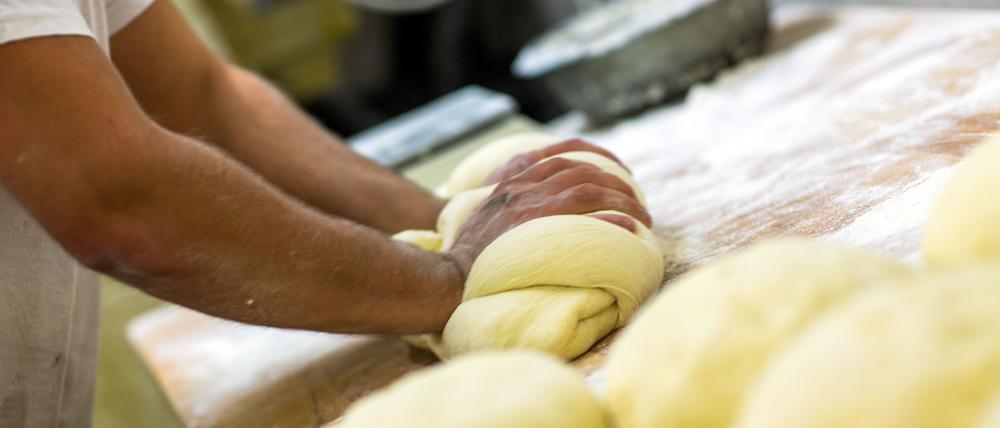 Ein Bäcker knetet in der Backstube einer Bäckerei Brotteig. (Symbolbild)