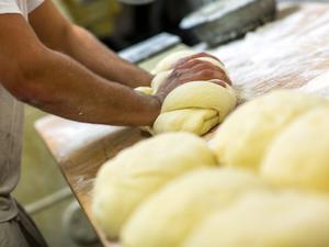 Ein Bäcker knetet in der Backstube einer Bäckerei Brotteig. (Symbolbild)
