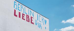 Ein blau-rotes Graffito mit der Aufschrift „Berlin Ick liebe Dir“ steht auf einer weißen Wand eines hohen Gebäudes, dahinter blauer Himmel und ein, zwei Wölkchen.