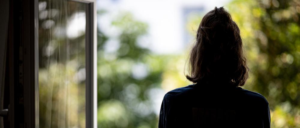 Eine Frau steht in ihrer Wohnung an einem Fenster.