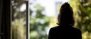  Eine Frau steht in ihrer Wohnung an einem Fenster.