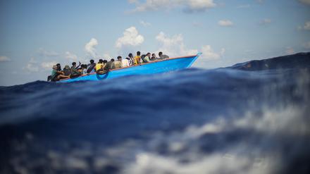 Migranten sitzen in einem Holzboot im Mittelmeer. 