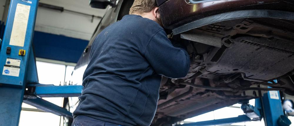 Ein Mechaniker schaut in einer Kfz-Werkstatt in den Radkasten eines Autos.