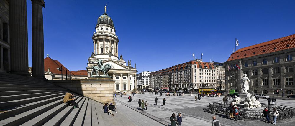 Bei Sonnenschein sind zahlreiche Menschen auf dem Gendarmenmarkt mit dem Konzerthaus (l) und dem Französischen Dom unterwegs.