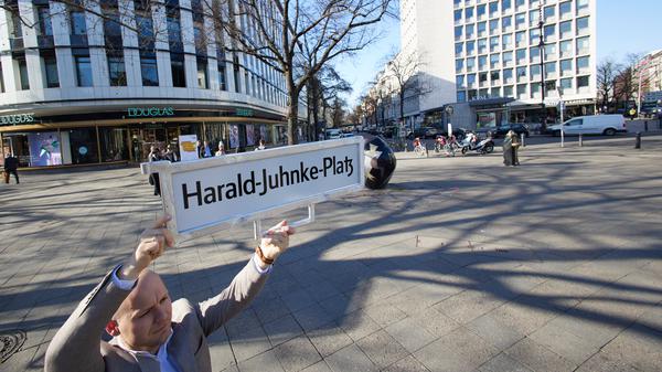 Felix Recke-Friedrich (FDP), Fraktionsvorsitzender in der Bezirksverordnetenversammlung Charlottenburg-Wilmersdorf, steht mit einem Straßenschild und der Aufschrift „Harald-Juhnke-Platz“ an der Straßenecke Kurfürstendamm/Uhlandstraße/Grolmanstraße.