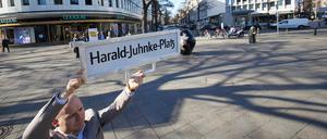 Felix Recke-Friedrich (FDP), Fraktionsvorsitzender in der Bezirksverordnetenversammlung Charlottenburg-Wilmersdorf, steht mit einem Straßenschild und der Aufschrift „Harald-Juhnke-Platz“ an der Straßenecke Kurfürstendamm/Uhlandstraße/Grolmanstraße.