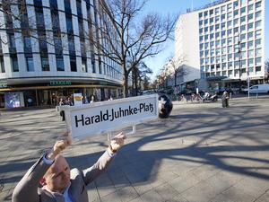 Felix Recke-Friedrich (FDP), Fraktionsvorsitzender in der Bezirksverordnetenversammlung Charlottenburg-Wilmersdorf, steht mit einem Straßenschild und der Aufschrift „Harald-Juhnke-Platz“ an der Straßenecke Kurfürstendamm/Uhlandstraße/Grolmanstraße.