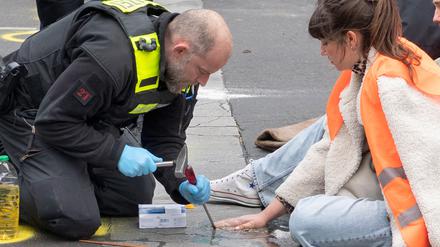 Polizeikräfte versuchen bei einer Straßenblockade der „Letzten Generation“, Carla Hinrichs, Sprecherin der Umweltschutzgruppe, von der Straße zu lösen.