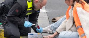 Polizeikräfte versuchen bei einer Straßenblockade der „Letzten Generation“, Carla Hinrichs, Sprecherin der Umweltschutzgruppe, von der Straße zu lösen.