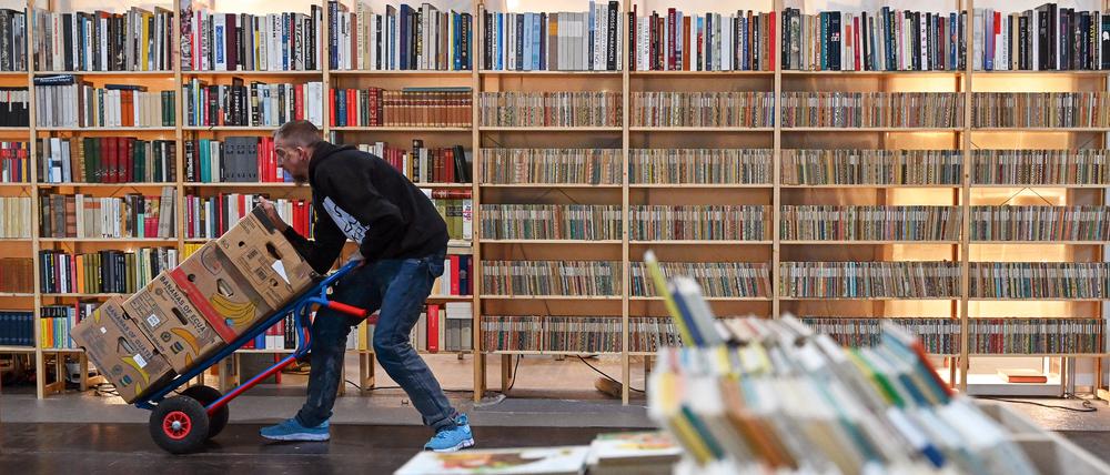 Letzte Vorbereitungen. Ein Mann schiebt auf einer Sackkarre Kartons mit Büchern vor sich her. Im Hintergrund ist ein Bücherregal der Antiquariatsmesse der Leipziger Buchmesse zu sehen.