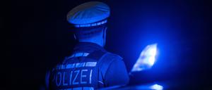 Ein Polizist steht an einem Polizeiauto mit Blaulicht.