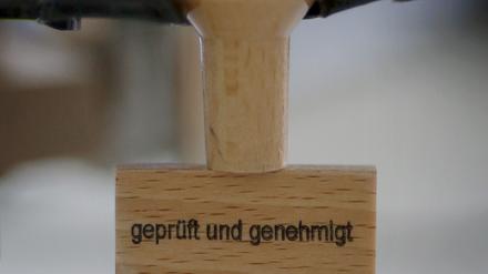 Am Platz eines Entscheiders steht am 03.08.2015 in der Außenstelle des Bundesamts für Migration und Flüchtlinge (BAMF) in Bingen am Rhein (Rheinland-Pfalz) ein Stempel mit der Aufschrift «geprüft und genehmigt». In der neuen Außenstelle des BAMF in Bingen wird über die Asyl-Anträge von Flüchtlingen entschieden. Foto: Fredrik von Erichsen/dpa (zu dpa "Asylanhörung: Fünf Stempel und Taschentücher für Flüchtlinge" vom 07.08.2015) +++ dpa-Bildfunk +++