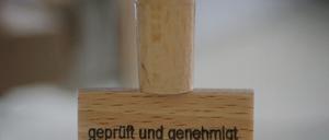 Am Platz eines Entscheiders steht am 03.08.2015 in der Außenstelle des Bundesamts für Migration und Flüchtlinge (BAMF) in Bingen am Rhein (Rheinland-Pfalz) ein Stempel mit der Aufschrift «geprüft und genehmigt». In der neuen Außenstelle des BAMF in Bingen wird über die Asyl-Anträge von Flüchtlingen entschieden. Foto: Fredrik von Erichsen/dpa (zu dpa "Asylanhörung: Fünf Stempel und Taschentücher für Flüchtlinge" vom 07.08.2015) +++ dpa-Bildfunk +++