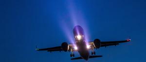 Ein Passagierflugzeug ist am Abend mit bereits ausgefahrenem Fahrwerk und Scheinwerferlicht im Landeanflug auf den BER Hauptstadtflughafen.