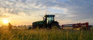 Ein Traktor steht vor der aufgehenden Sonne auf einem Feld. Auch Ernährung und damit verbundene Nutzflächen sind maßgebende Faktoren für den Klimawandel.
