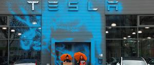 Vor der mit blauer Farbe besprühten Front des Tesla-Centers in Reinickendorf stehen zwei Frauen mit orangen Regenschirmen.    