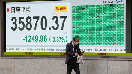 Ein Fußgänger geht an einem Bildschirm vorbei, der den japanischen Nikkei-Aktiendurchschnitt in Tokio anzeigt.