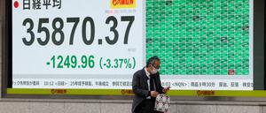 Ein Fußgänger geht an einem Bildschirm vorbei, der den japanischen Nikkei-Aktiendurchschnitt in Tokio anzeigt.