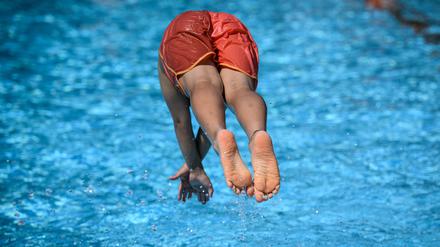 Ein Junge springt im Sommerbad Neukölln ins Schwimmbecken.