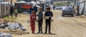 ARCHIV - 21.02.2025, Palästinensische Gebiete, Al Mawasi: Kinder tragen Töpfe mit Lebensmitteln vor Zelten von vertriebenen Palästinensern in Al Mawasi. Israel verhindert nach wie vor die Zufahrt von mobilen Unterbringungsmöglichkeiten für vertriebenen Palästinenser, deren Häuser von der israelischen Armee vor ihrem Rückzug aus einigen Städten des Gazastreifens zerstört wurden. (zu dpa: «Unicef: 322 Minderjährige bei neuen Angriffen in Gaza getötet») Foto: Abed Rahim Khatib/dpa +++ dpa-Bildfunk +++