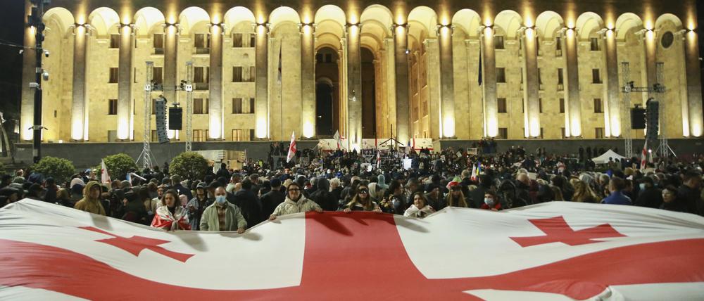 dpatopbilder - 31.03.2025, Georgien, Tiflis: Demonstranten mit einer riesigen georgischen Nationalflagge versammeln sich vor dem georgischen Parlamentsgebäude, um die Freilassung politischer Gefangener und Neuwahlen zu fordern. Foto: Zurab Tsertsvadze/AP/dpa +++ dpa-Bildfunk +++