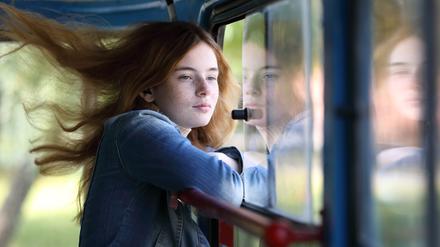 Eine junge Frau steht mit wehenden Haaren an einem offenen Fenster.