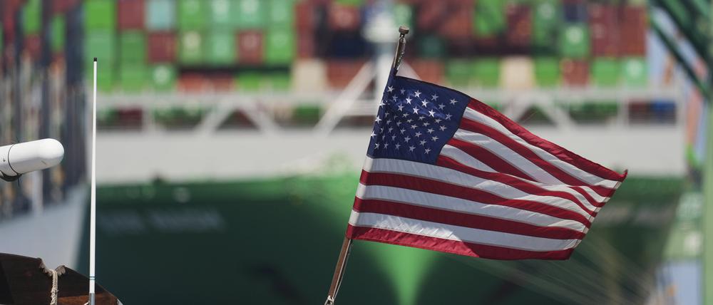Eine US-Flagge weht vor einem Containerschiff im Hafen von Los Angeles.