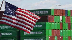 Container sind im Hafen von Los Angeles gestapelt während im Vordergrund eine US-Flagge weht.