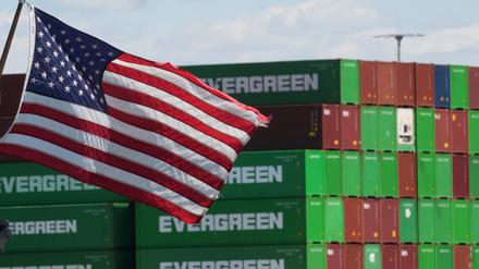Container sind im Hafen von Los Angeles gestapelt während im Vordergrund eine US-Flagge weht.
