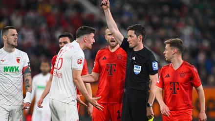 Schiedsrichter Matthias Jöllenbeck zeigt Augsburgs Cédric Zesiger nach einem Zweikampf mit Harry Kane Gelb-Rot.