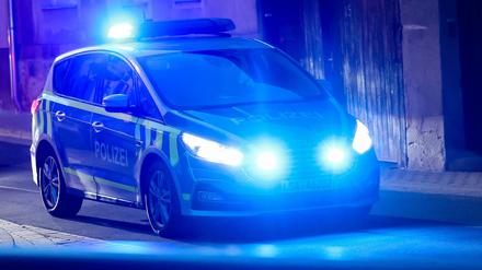 Ein Fahrzeug der Polizei fährt mit Blaulicht am Abend durch eine Straße. 