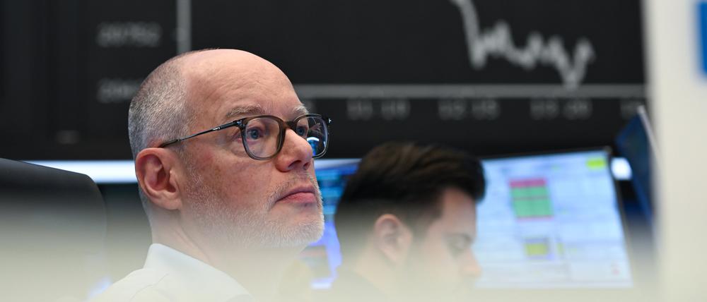 Börsenhändler beobachten auf dem Parkett der Frankfurter Wertpapierbörse ihre Monitore, während die Anzeigetafel mit der Dax-Kurve fallende Kurse anzeigt. 