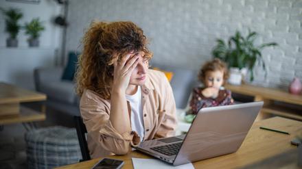 Eine Frau vorm Laptop versucht zu arbeiten, während ihr Kleinkind neben ihr sitzt (Symbolbild).