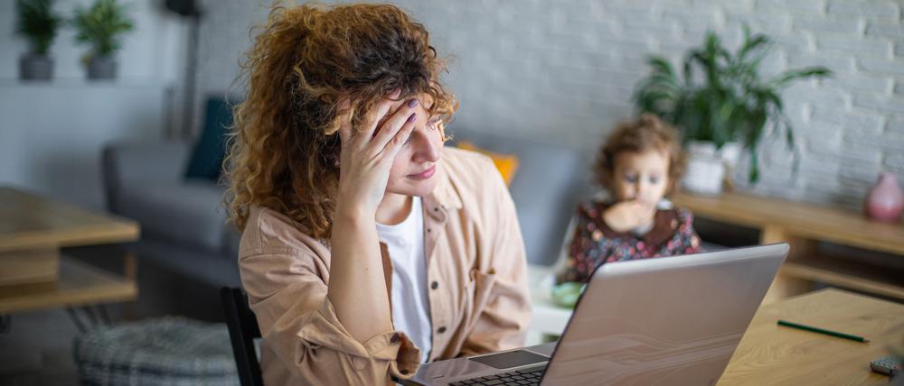 Eine Frau vorm Laptop versucht zu arbeiten, während ihr Kleinkind neben ihr sitzt (Symbolbild).