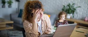 Eine Frau vorm Laptop versucht zu arbeiten, während ihr Kleinkind neben ihr sitzt (Symbolbild).