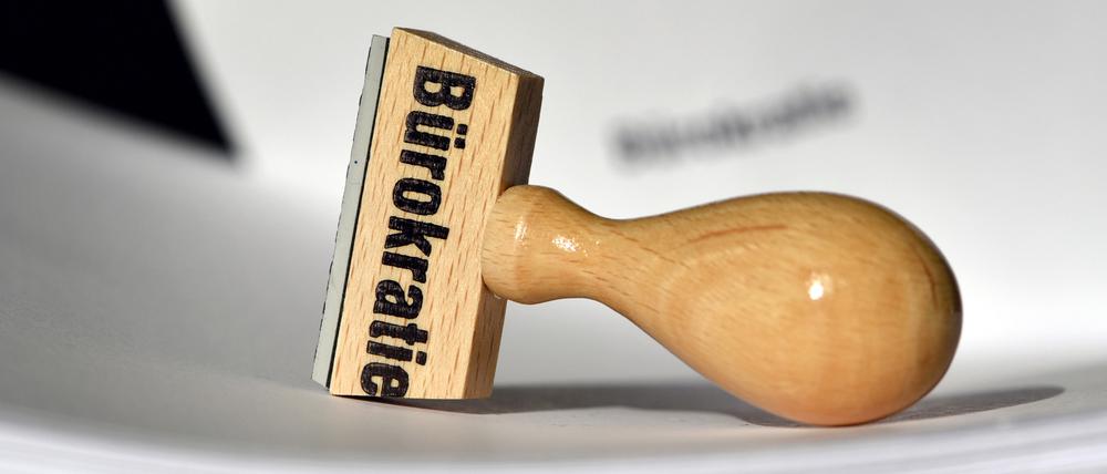 Ein Stempel mit der Aufschrift „Bürokratie“ liegt auf Papieren. 