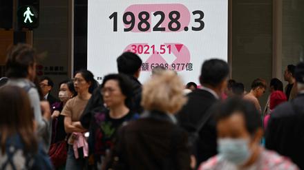 Passanten in Hongkong vor einer Leuchtanzeige mit dem Hang-Seng-Index. 