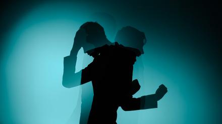 Zweigeteilter Schatten eines Mannes. Einer hält sich die Hand an den Kopf, der andere reckt wütend die Faust.