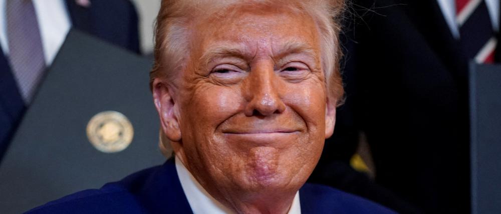 Donald Trump unterzeichnet mit einem Grinsen ein Dokument im Weißen Haus.